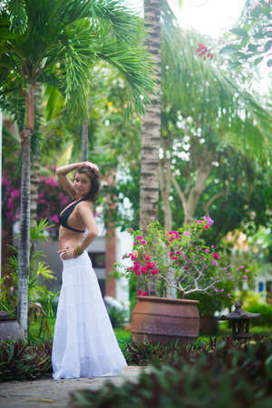Young beautiful girl in a white skirt and black bra posing on a background of palm trees in the summerの写真素材
