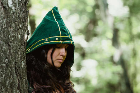 Staging photo of beautiful woman in fantasy suit with hood in forestの写真素材