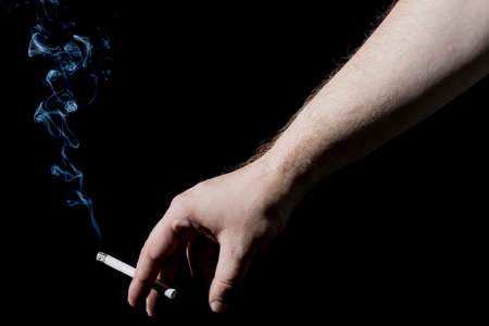 Man's Hand Holding a Smoking Cigarette on Black Background. Close up with White Cigarette Smoke