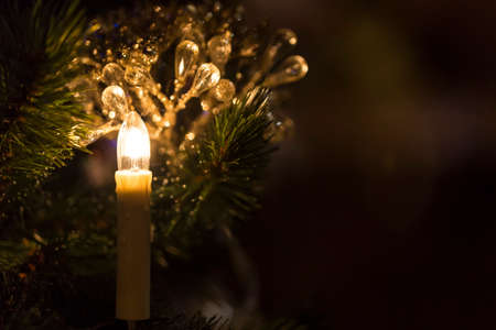 Christmas toy candle in front of a Christmas tree with sparkling lights on dark background