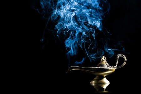 Magic lamp on black background from the story of Aladdin with Genie appearing in blue smoke concept for wishing, luck and magicの写真素材