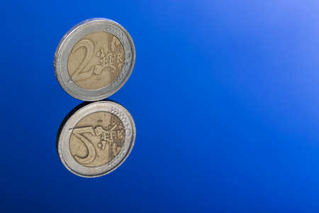 Closeup of two Euro coin on blue background with nice reflection and free space for text.