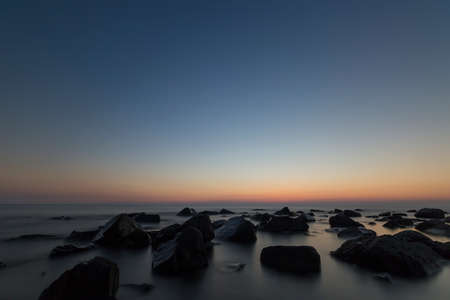 Sunset over the coast with stones with blurred waterの写真素材