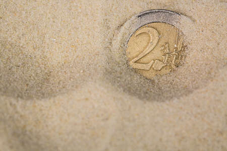 Finance concept. Euro coin swamps in the sand.