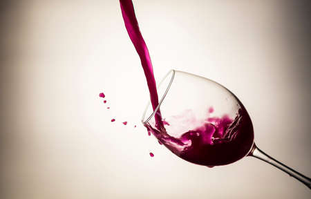 Red wine pouring in a wineglass with wine drops on light backgroundの写真素材