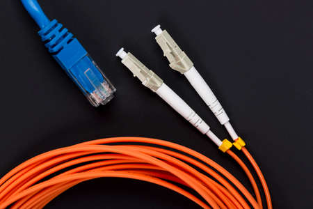 Blue twisted pair patch cord with fiber optics orange cable on dark background.