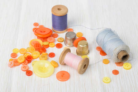 Different thread spools with colorful buttons and thimbles on light surface.の写真素材