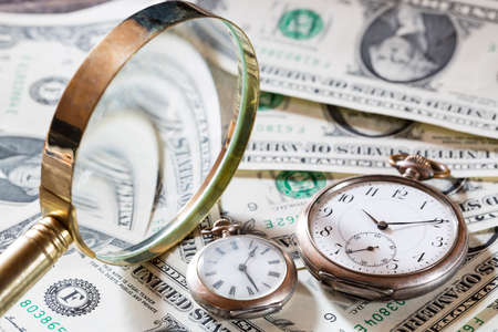 Time is money finance concept with old vintage clocks, dollar bills and magnifying glass.