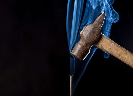Metal rusty hammer above nail with smoke on black background.の写真素材
