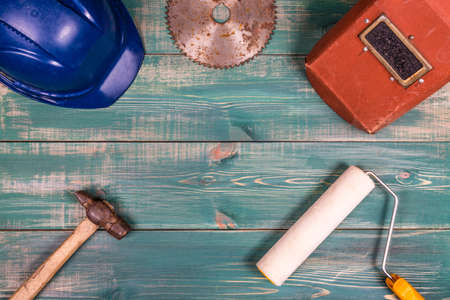 Construction concept. Roller, hammer, hard hat, circular saw blade and welding mask on nice green wood background.の写真素材