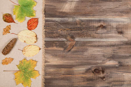 Autumn leaves over burlap texture with wooden background and copy spaceの写真素材