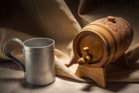 Wooden barrel with vintage iron mug on canvas background.の写真素材