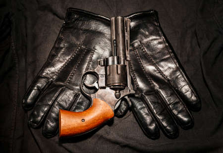 Crime concept. Black gun with leather gloves on dark cloth.