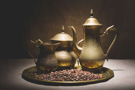 Vintage still life with heap of coffee beans near old copper coffeepots on bronze tray against canvas background.の写真素材