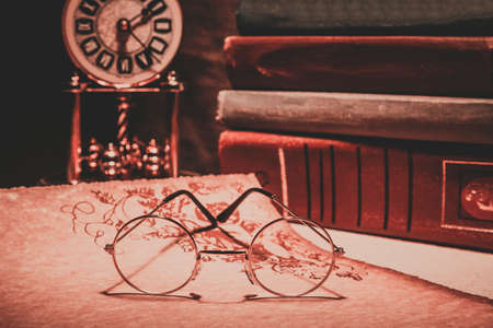 Old glasses on scroll with books and old clock. Vintage toned photoの写真素材