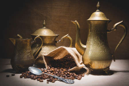 Heap of coffee beans in burlap sack with a vintage spoon and different vintage turkish coffeepots on canvas background.の写真素材