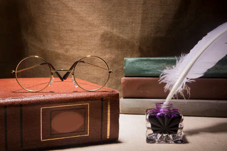 Vintage still life with glasses on old book near inkstand and feather on canvas background.の写真素材