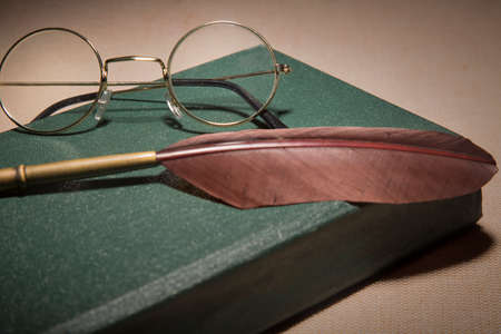 Closeup of fountain feather pen with vintage glasses on old green book. Selective focus.の写真素材