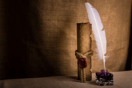 Literature concept. Old inkstand with feather near scroll and on canvas background.の写真素材