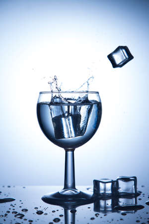 Ice cubes falling in glass with water splashesの写真素材
