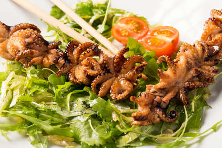 Barbecue baby octopus on white plate with herbs, tomatoes and sticks.の写真素材