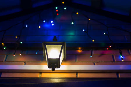 Glowing colorful Christmas lights and lamp at the house entrance.