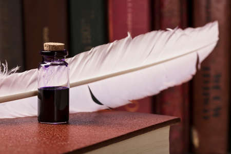 Vintage still life with inkwell near quill on old book on books background.の写真素材