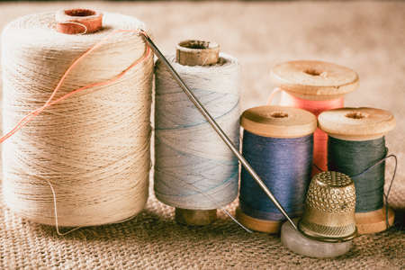 Collection of color thread spools with needle and thimble on canvas background. Vintage toned photo.の写真素材
