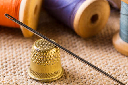 Sewing concept. Needle with thimble close up near thread spools on canvas background.の写真素材