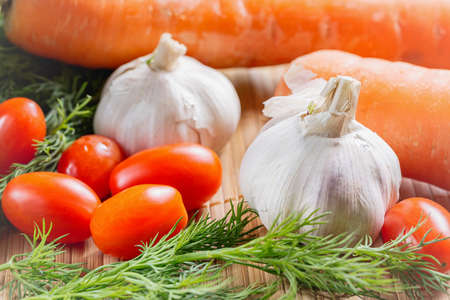 Vegetables on bamboo table cloth. Fresh cherry tomatoes, garlic, carrot, dill close up.の写真素材