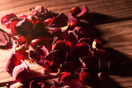 Many red rose petals on wooden background under beam of light with shadowsの写真素材