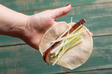 Woman hand holding pancake with Pekin Duck meat, onions and cucumbr pieces. Top view.