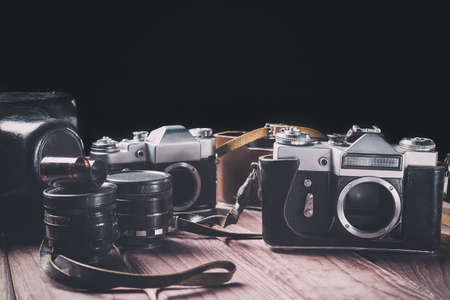 Old film cameras with lenses and cases on wood against black background. Vintage toned and selective focus.の写真素材