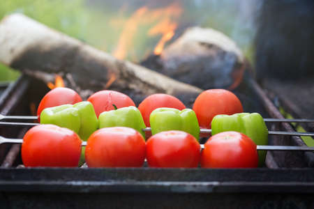 Grilling tomatoes and paprika on skewers with fire outdoors. Selective focus on paprika.の写真素材