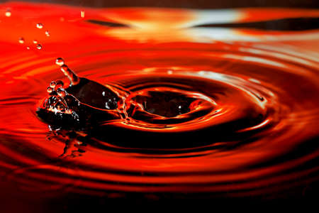 Abstract picture of water drop with splash and ripples on nice red orange background.の写真素材