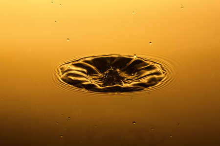 Abstract picture of fallen water drop with splash and ripples on nice gradient orange yellow background.の写真素材