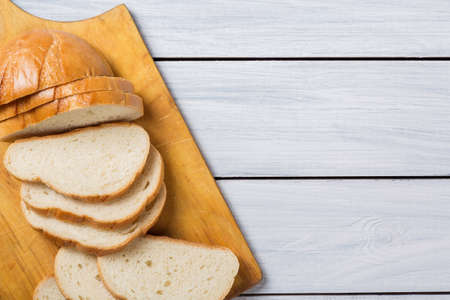 Fresh bread slices on cutting board against white wooden background. Top view.の写真素材