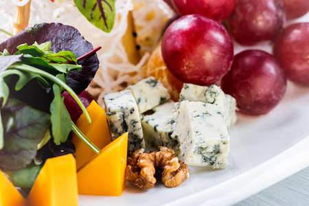 Restaurant cheese plate - various types of cheeses with grapes and walnut on white plate. Close up image with selective focus.の写真素材