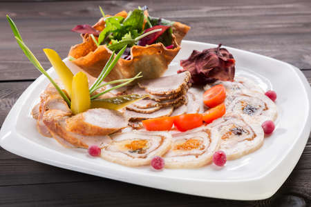 Meat plate with delicious pieces of sliced ham, cherry tomatoes, herbs, meat and cucumber with cranberry on wooden table.の写真素材