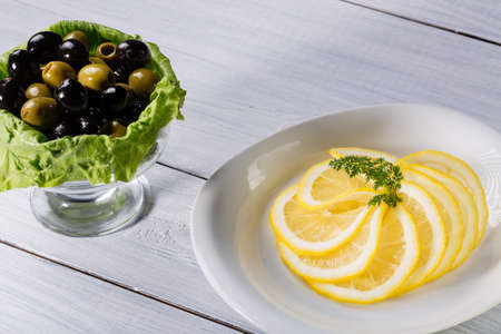 Sliced lemon pieces with olives on white wooden table.の写真素材