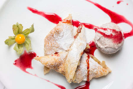 Apple strudel with ice cream, cape gooseberry and fruit spread on white plate