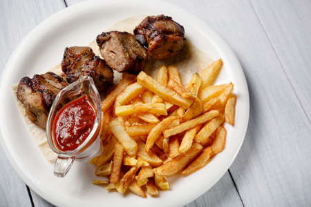 Grilled shish kebab served with french fries and sauce on white wooden table.の写真素材