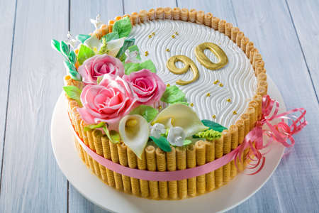 Delicious cake with roses, lily, leaves and figures 90 Years on light blue wooden table close up with selective focus.の写真素材