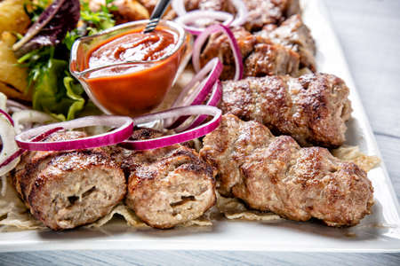 Lyulya kebab with red sauce and onion on white plate close up with selective focus.の写真素材