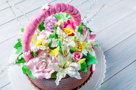 Delicious cake basket with various flowers on white wooden table. Selective focus.