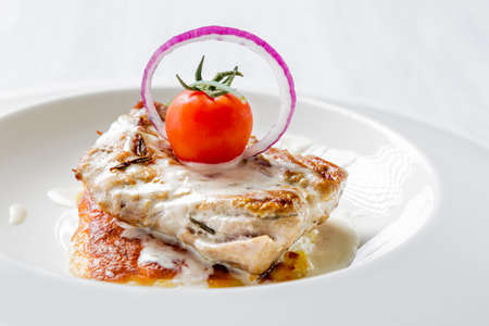 Tasty roasted pork pieces with cheese sauce, tomato and onion on white plate close up. Selective focus image.の写真素材
