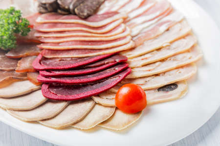 Meat plate with delicious pieces of sliced ham, cherry tomatoes and meat. Close up with selective focus.の写真素材