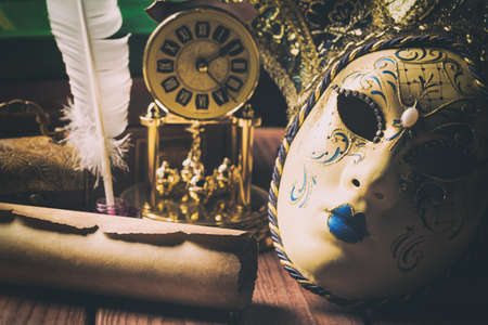 Literature concept. Still life with feather in inkstand, scroll, venetian mask, old books,vintage clock and box on wooden table. Vintage toned image.の写真素材