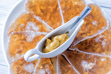 Jellied meat with mustard in a bowl and spoon on white plate close up.の写真素材