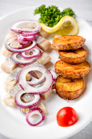 Plate of pieces of herring with fried potato,onion, tomato and lemon. Close up image with selective focus.の写真素材